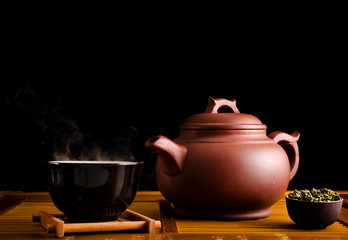 Chinese tea ceremony. Ceramic tea pot and cups with the famous chinese oolong tea Tieguanyin  with vapour on a black background.