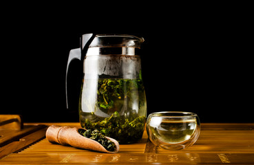 Chinese tea ceremony. Glass jug with green oolong tea Tieguanyin on a black background with a scoop of tea and a glass cup of tea. 