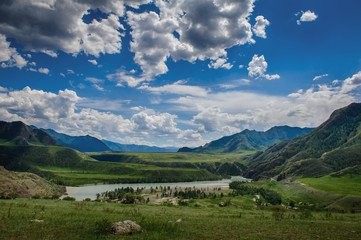 Beautiful view from hill to the confluence of two rivers under a blue sky with clouds in the Altai mountains. Amazing landscape of green valley on a sunny summer day.