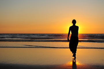 Silhouette of young girl on the background of sunset by the sea. Figure of a woman in the rays of setting sun. Beautiful sunset, touchdown and a girl walking on seashore.