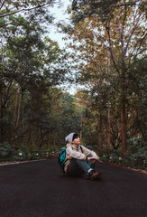 Asian young man in boots on sitting the road in mountains with enjoying their alone forest outdoor active lifestyle travel adventure, people hiking vacations in Thailand.