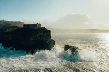 Nazare Portugal giant waves hitting cliffs rocks and lighthouse from above view drone