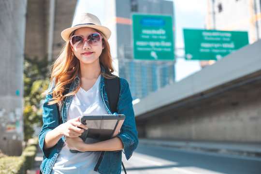 Happy Asian woman traveler holding a mobile phone in station and waiting for train in vacation time. Young Asian Tourists With Backpacks Train travel in Sightseeing City Thailand.