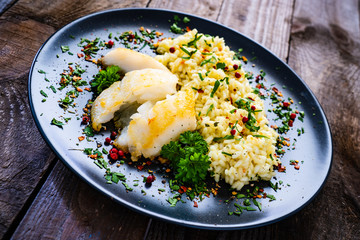 Risotto with fried cod loin on wooden background