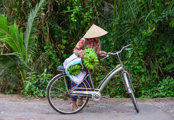 Fototapeta na wymiar An old woman carrying banana by her bicycle