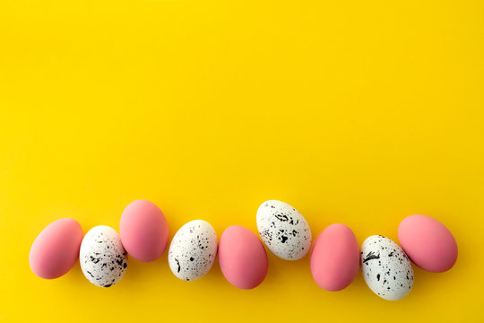 Flat lay top view of white and pink eggs with minimal designs on yellow background