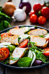 Caesar salad - barbecue chicken breast and vegetables on wooden table