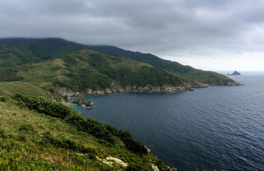 Beautiful seascape - green hills, sea, island on the horizon under a cloudy sky.