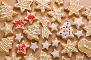 Christmas beautiful gingerbread cookies in white icing glaze with red stars, snowflakes and spruce tree on wooden table background, flat lay