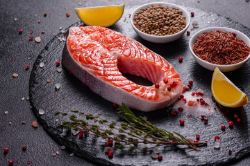 Raw trout red fish steak served with herbs and lemon and olive oil on a dark background