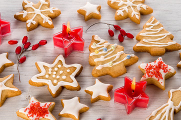 Beautiful homemade Christmas cookies with white icing, red candles and berries on wooden background, close-up