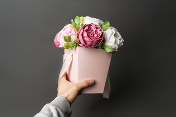 Flowers in bloom: A bouquet of lilac and white peonies in a pink box in a male hand.