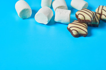 Scattered striped white and dark chocolate candies in shape of star and marshmallow in form of...