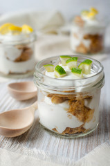 milk yogurt with cereal and slices of lemon in a glass jar with wooden spoons on a wooden light background, light diet breakfast, healthy food