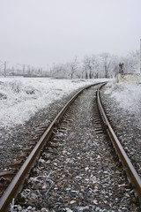 A railroad line running along a white cement fence that is covered with fluffy white snow in winter.