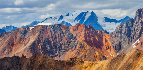 Obraz premium Colored cliffs and snow-capped peaks. Cloudy weather and morning light. Panoramic view.