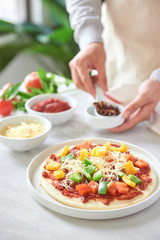 Baker's hand placing ingredients on pizza