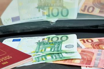 Euro banknotes and red passport on the dashboard and their reflection in the windshield inside of a car
