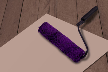 Paint brush roller on white paper and wooden background. Purple used paint tool as a concept of...