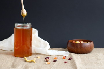 Honey in glass container and dried fruits in wooden bowl