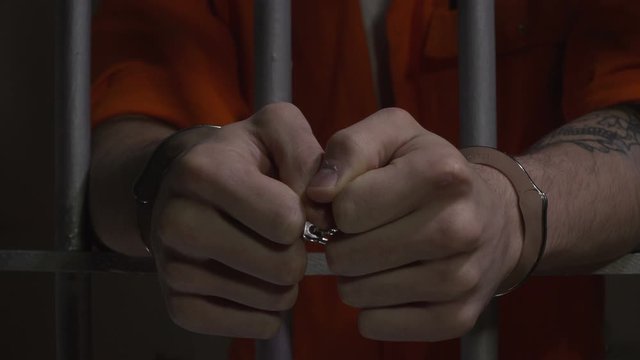 Handcuffs on male Prisoner or Inmate in Jail / Prison Cell. Close up Dolly shot. Orange. 