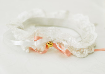 White lace garter for the bride with a coral satin ribbon and a gold heart on a white background