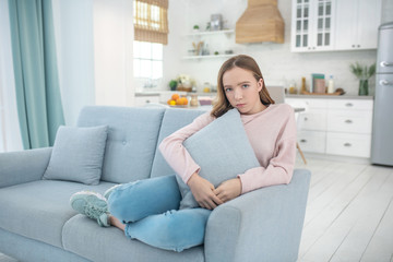 Sad girl sitting on a sofa at home.