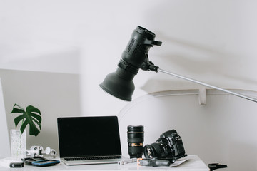 Still life working from home desk with professional photographic equipment, camera, lens, computer monitor, electronics indoors.