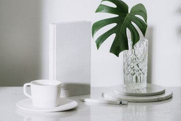 Monstera tropical palm leaves in a glass vase standing on office table with stationary