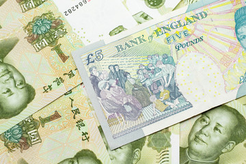 A close up image of a multicolored five pound note from the United Kingdom on a background of Chinese one yuan bills in macro
