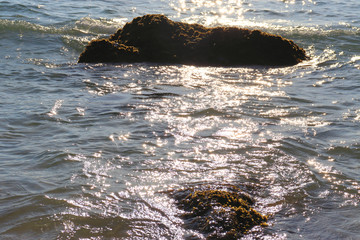 Beach idyll, sand and stones, bright sun glare on the waves