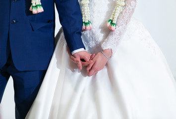 Bride and Groom in formal costumes with flower garlands, looking nervous, holding hands on the stage in traditional Thai wedding reception ceremony. Life Event, Marriage, Moment and Emotion concept