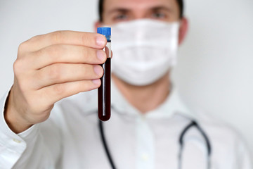 Test tube in male hand close up, doctor in medical mask holding a vial with red liquid. Concept of...