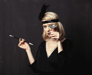 Beautiful blonde woman in twenties years clothes with smoking pipe and cocktail on dark background