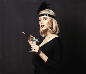 Beautiful blonde woman in twenties years clothes with smoking pipe and cocktail on dark background