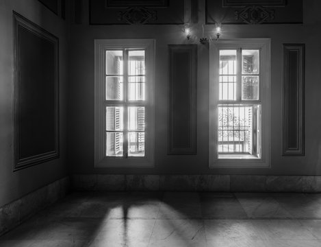 Black and white high contrast shot of two narrow windows, revealing strong light into dark room with white tiled marble floor 