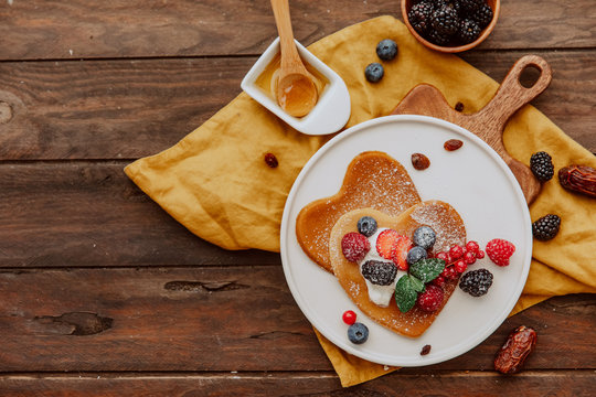 Homemade heart shaped pancakes with berries on wooden table. Breakfast or brunch for Valentine's Day.