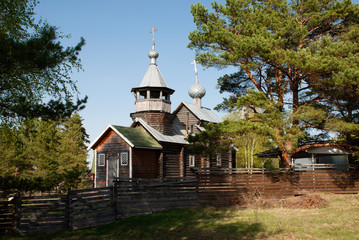 Fototapeta premium Wooden orthodox church behind the fence against the sky among the trees
