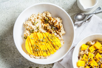 Oatmeal with mango and pumpkin seeds in white bowl, top view. Healthy breakfast, vegan food.
