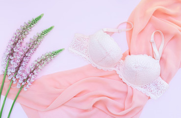 Delicate lace underwear on a pink background with pink lupine flowers. Pastel background. Flat lay, top view.