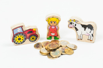 toy figurine of a woman cow and tractor next to a pile of Euro coins on a white background