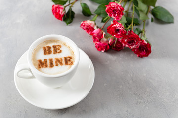 Romantic coffee with message be mine for St. Valentines Day and a Bouquet of roses on gray background. Copy space. Cafe, restaurant menu, recipe concept