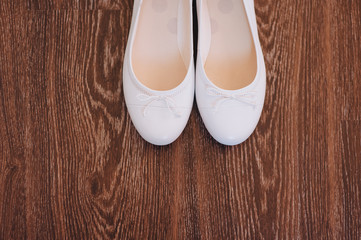 White wedding leather shoes stand on a background of brown wooden parquet. Photography, concept, top view, copy space.