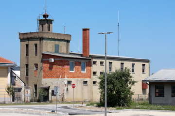 Back view of old dilapidated fire station with new red building blocks unfinished part and vintage retro siren on top surrounded with paved road and other buildings