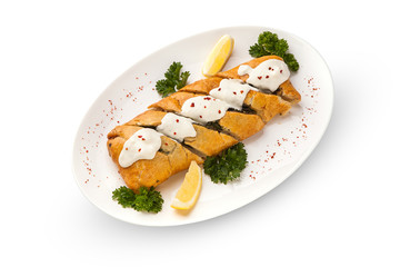 baked perch in puff pastry in the form of a pigtail with greens and slices of lemon, sprinkled with creamy sauce. Dough-coated fish with spinach on a white plate. White background, isolated