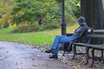 girl in a hat and a raincoat sits on a park bench