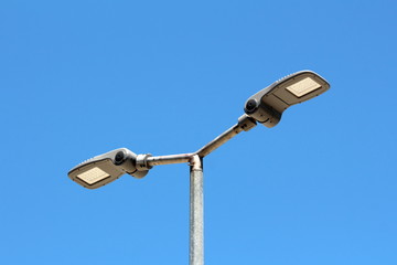 Dual modern LED street lights with adjustable angle mounted on single tall metal pole on clear blue sky background