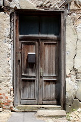 Leaning old dilapidated wooden doors with faded color mounted on abandoned suburban family house ruins cracked wall with destroyed facade and partially visible red bricks