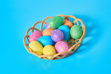 Full plastic basket of colorful eggs with glitters lies on blue table on kitchen. Easter concept. Close-up