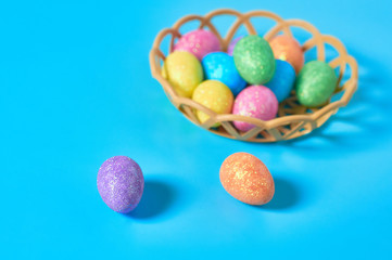 Full plastic basket of colorful eggs with glitters lies on blue table on kitchen. Easter concept. Close-up